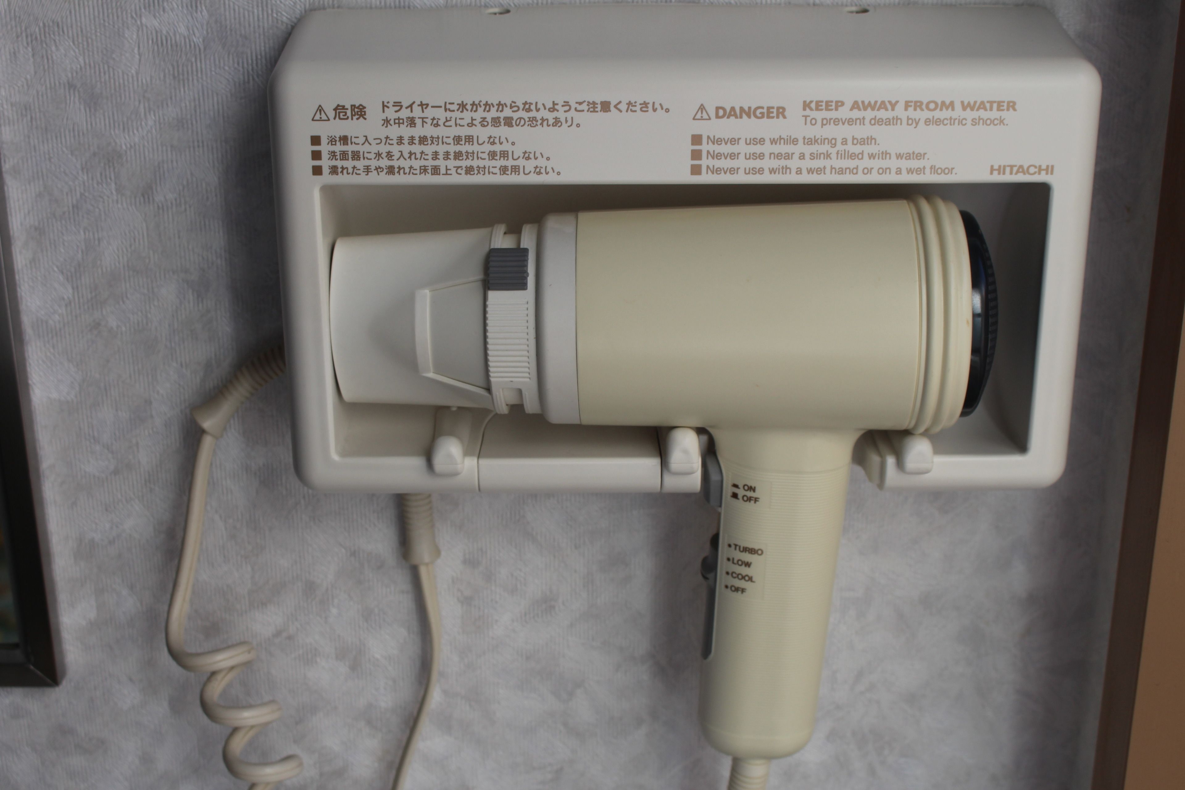 Un sèche-cheveux doté d’avertissements de sécurité et d’un panneau de commande avec les fonctions MARCHE/ARRÊT et TURBO/VITESSE LENTE/AIR FROID.