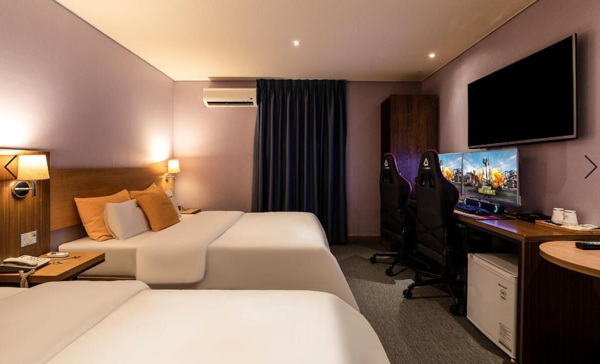 Une chambre d’hôtel avec deux lits, un bureau avec un ordinateur, une télévision et un appareil de climatisation.