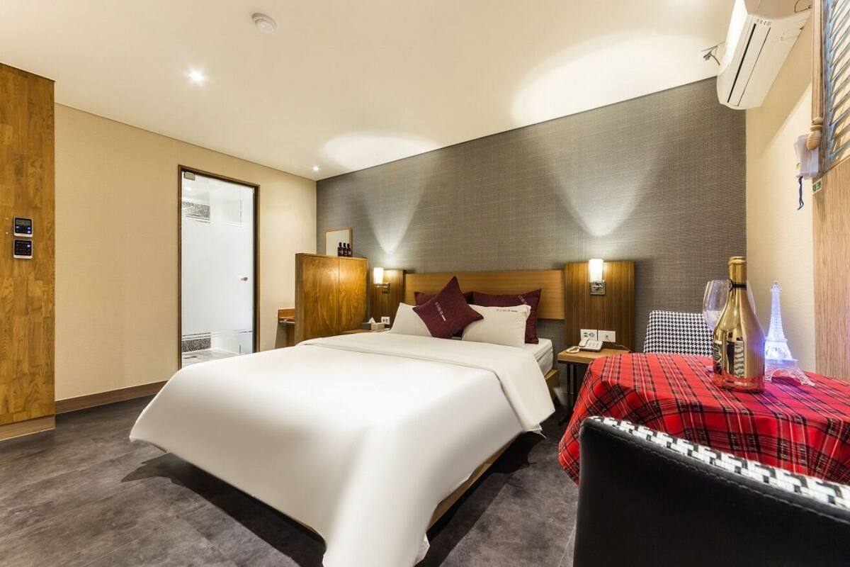 A hotel room with a large bed, a small table with a red checkered tablecloth, and a minibar.