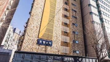 Un bâtiment d’hôtel avec une grande enseigne « HÔTEL » bien visible sur la façade, un grand panneau jaune vertical et une enseigne indiquant « Soma » à l’entrée.