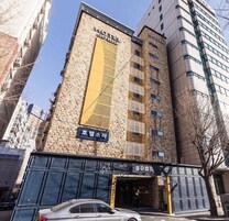 Un bâtiment d’hôtel avec une grande enseigne « HÔTEL » bien visible sur la façade, un grand panneau jaune vertical et une enseigne indiquant « Soma » à l’entrée.