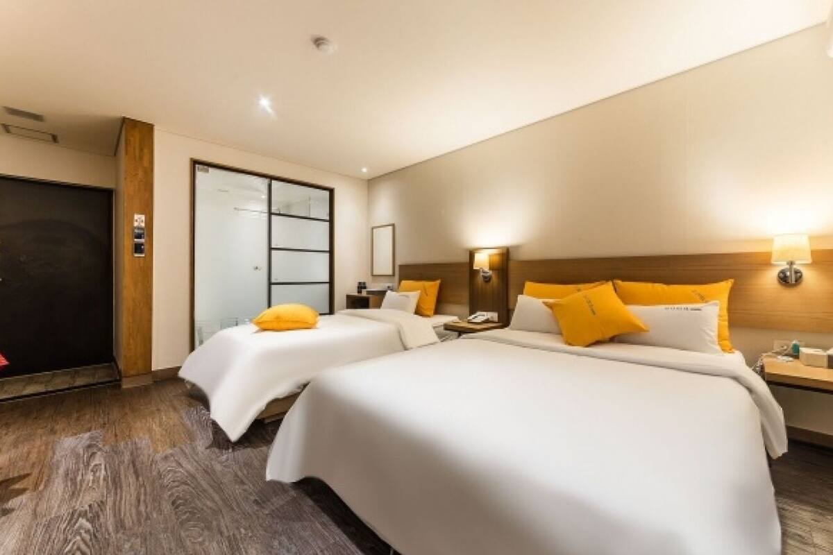 A hotel room with three beds, a wooden headboard, a desk, and a wardrobe.