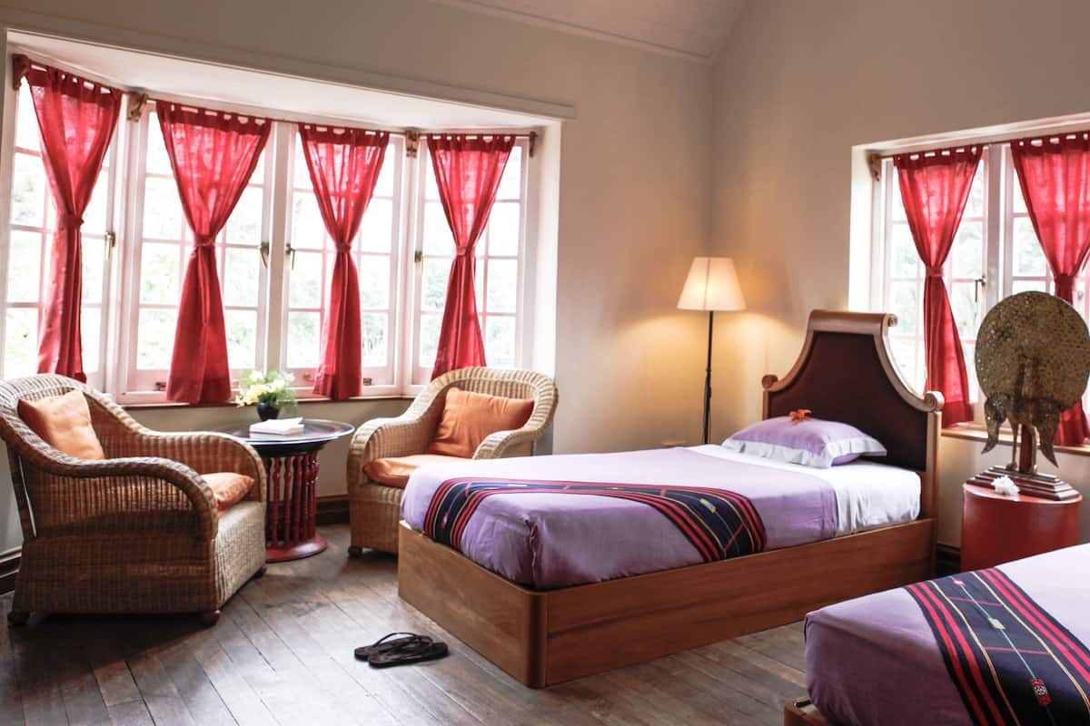 Ein Hotelzimmer mit zwei Betten, einem Sessel, einer Lampe und einem kleinen Tisch.
