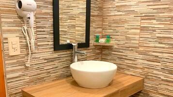A bathroom with a round sink, a hairdryer, a mirror, and a shelf with toiletries.