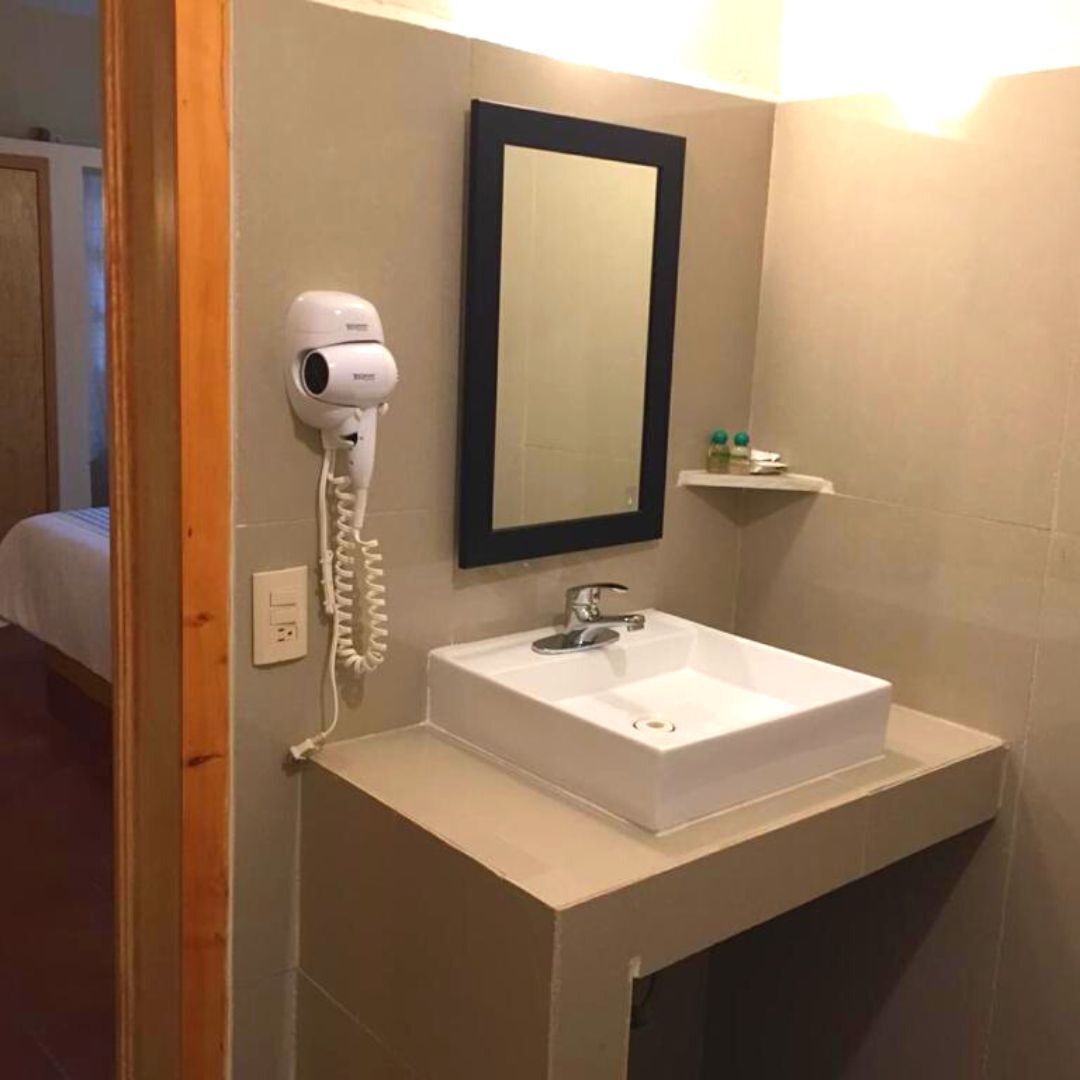 Un baño con un lavabo blanco, un secador de pelo, un espejo y un estante con artículos de aseo.