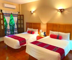 Dos camas individuales con sábanas blancas y almohadones rojos, cabeceros de madera, una mesita de noche con lámpara y una ventana con cortinas.