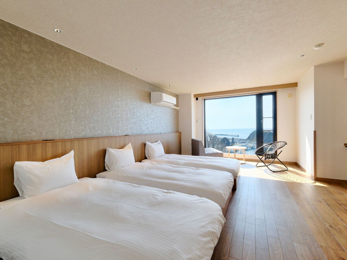 Una habitación de hotel moderna con tres camas, un ventanal grande y vistas a la ciudad.