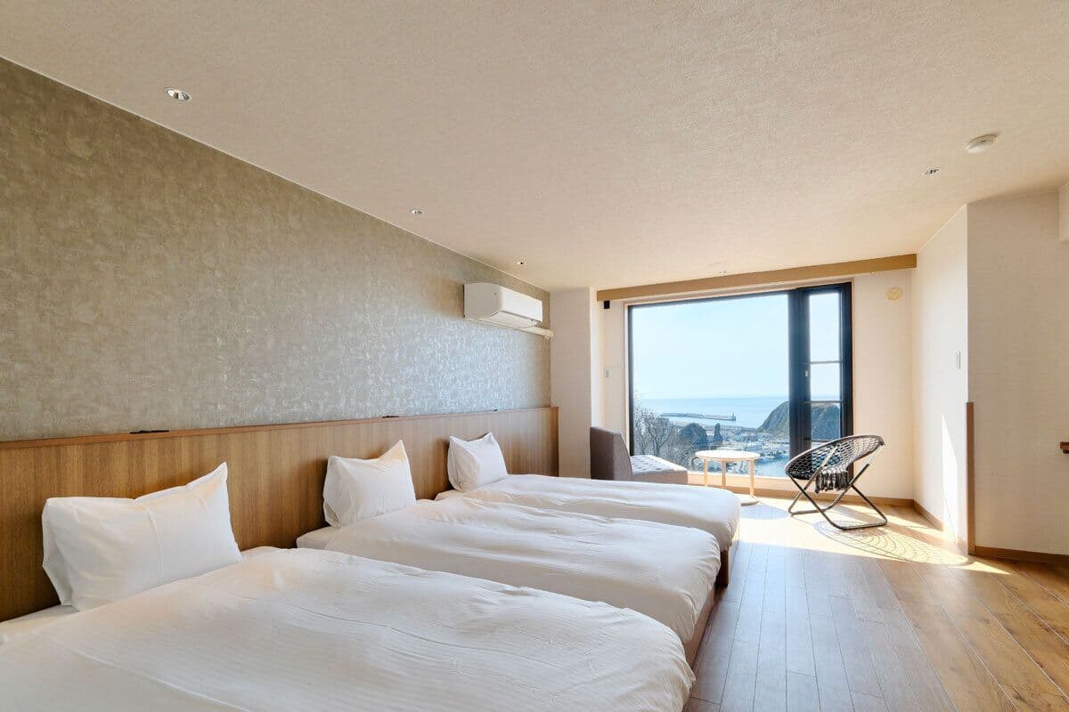 Una habitación de hotel moderna con tres camas, un ventanal grande y vistas a la ciudad.