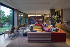 Un área de estar moderna con disposición de asientos, un mural grande y vistas al exterior.