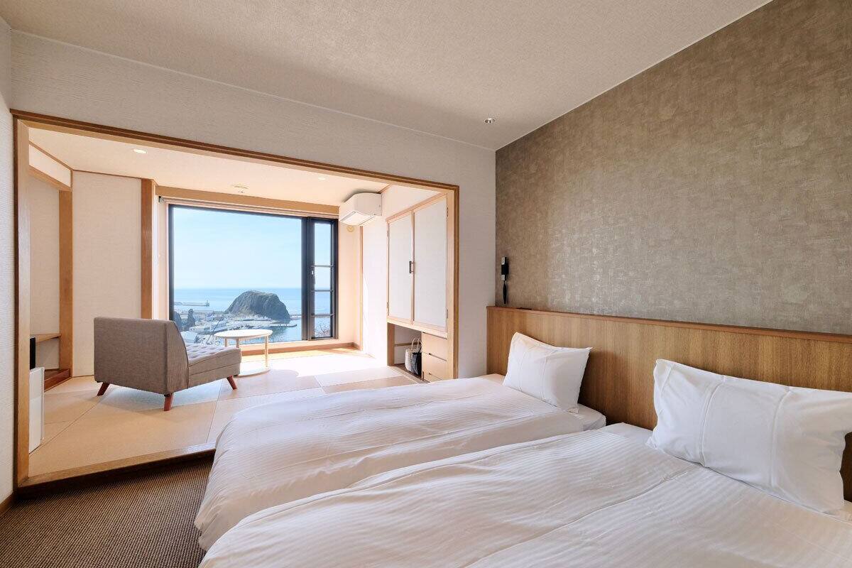 A hotel room with a large bed, a chair, and a view of the sea.