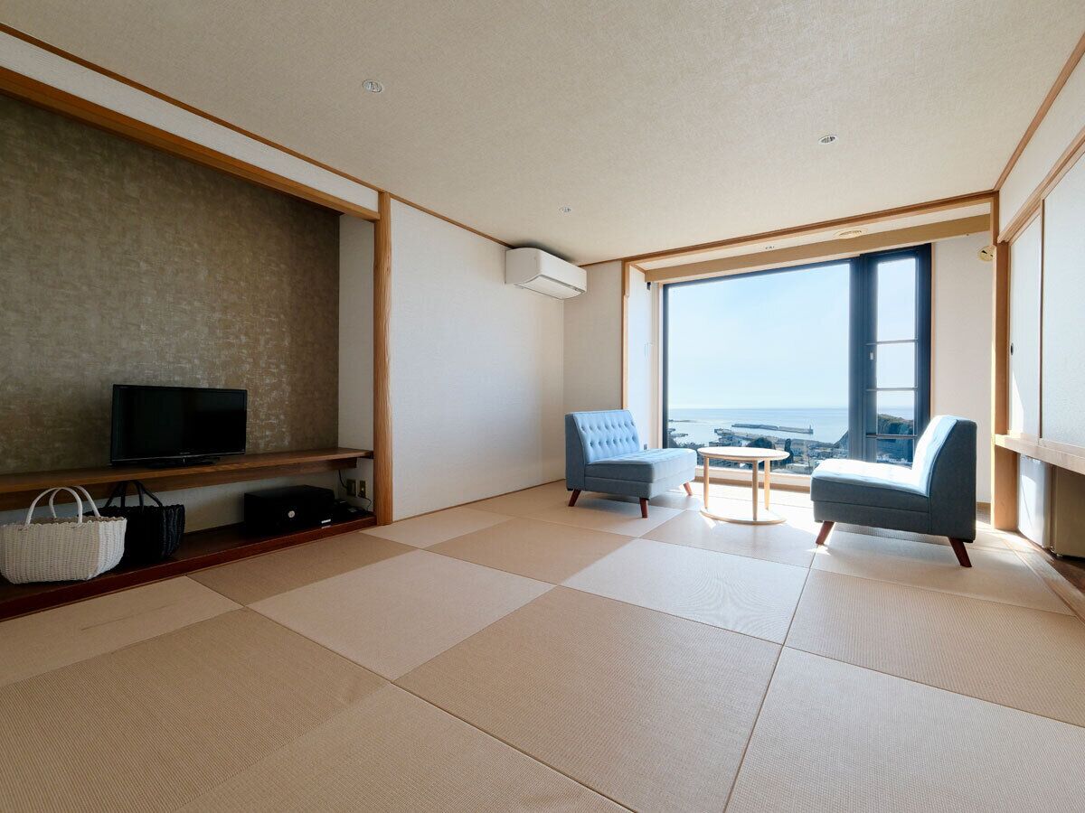 Una sala de estar moderna con suelo de tatami, televisor, sofá y vistas al mar.