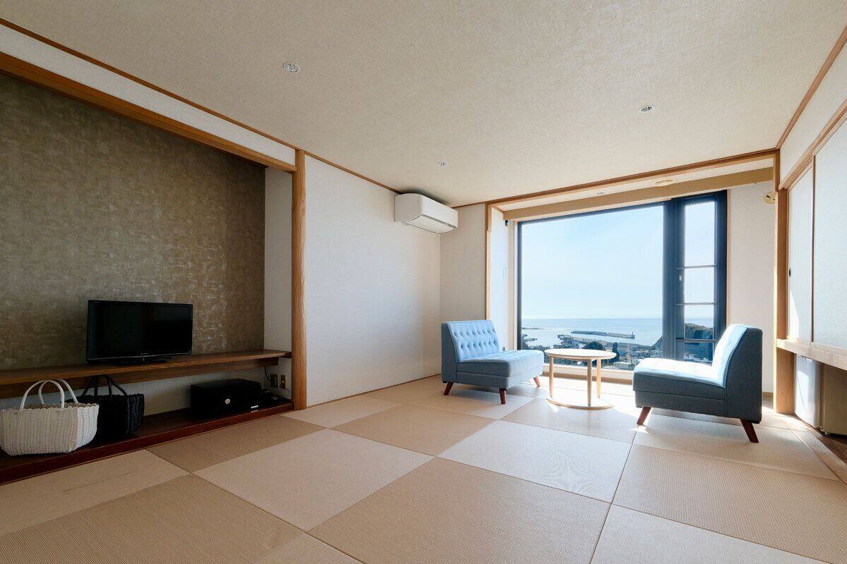 A modern living room with tatami flooring, a television, a sofa, and a view of the sea.