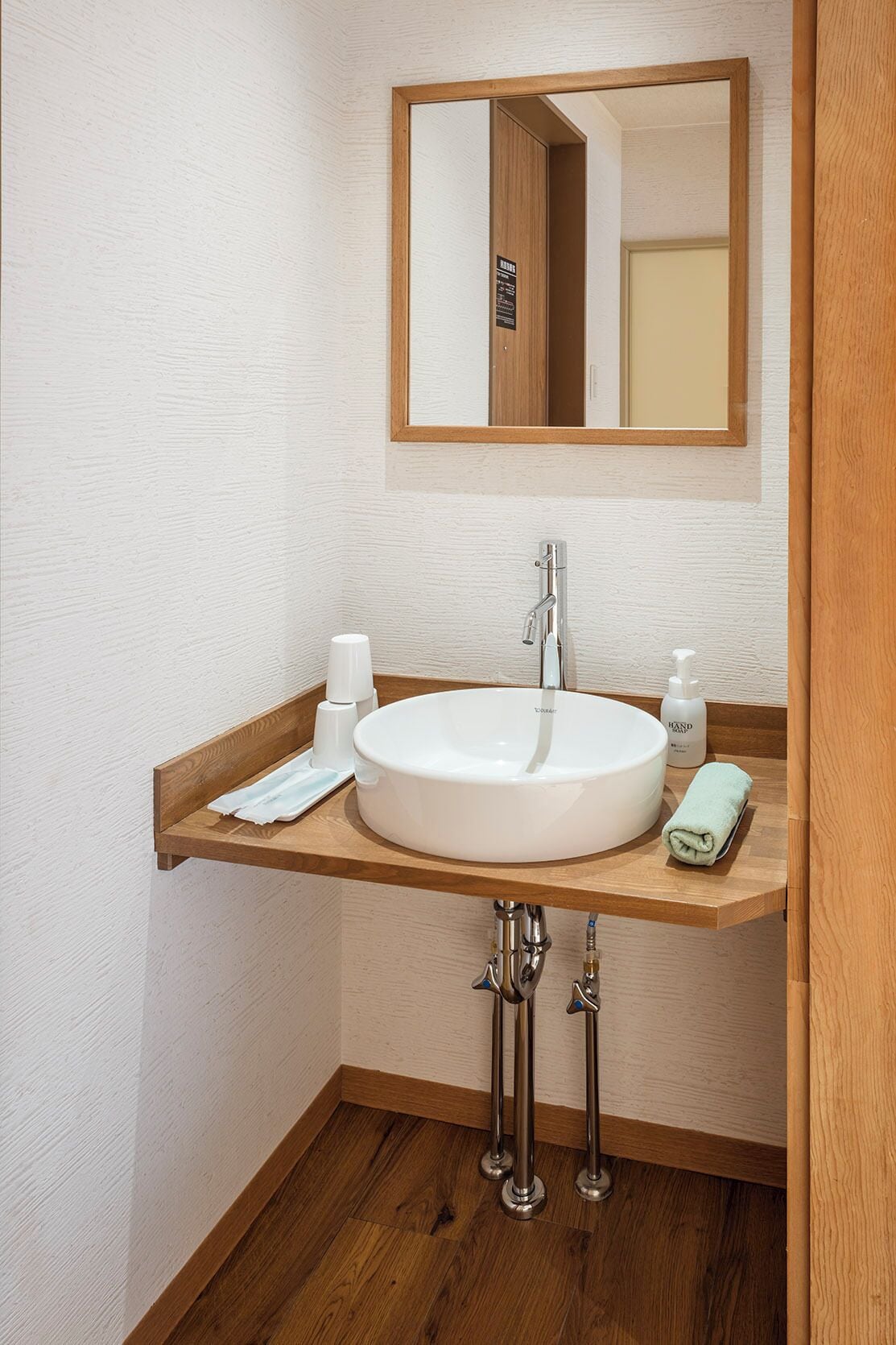 Ein Badezimmer mit einem weißen Waschbecken, einer Holzablage, einem Spiegel und einem Handtuch.