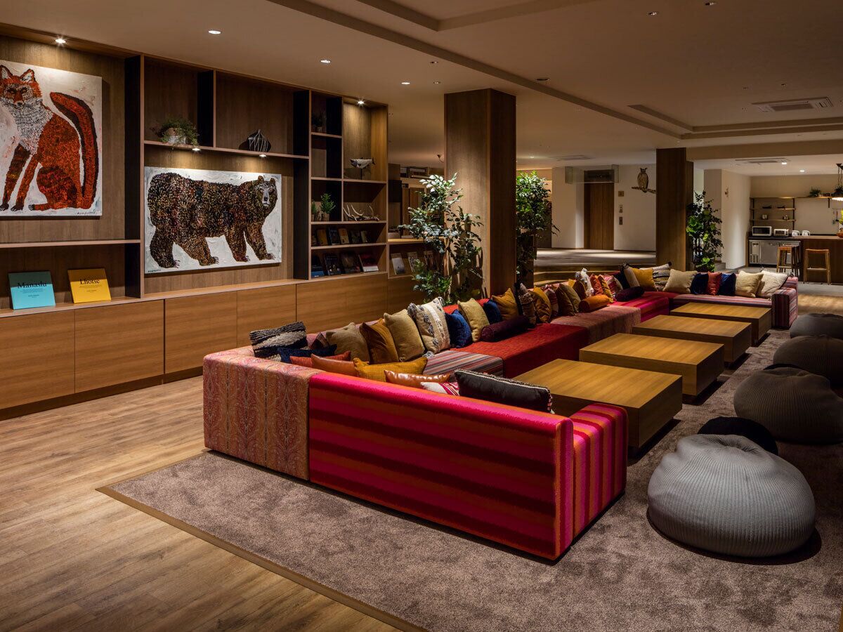 A modern living room with a long red sofa, a kitchen in the background, and a bookshelf with framed pictures.