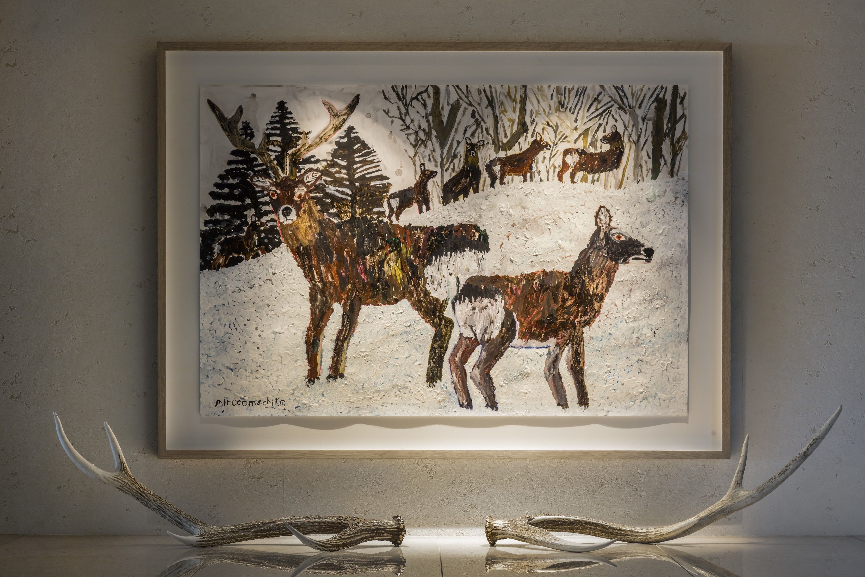 A framed wildlife painting with deer and trees, mounted on a wall with antlers in front.