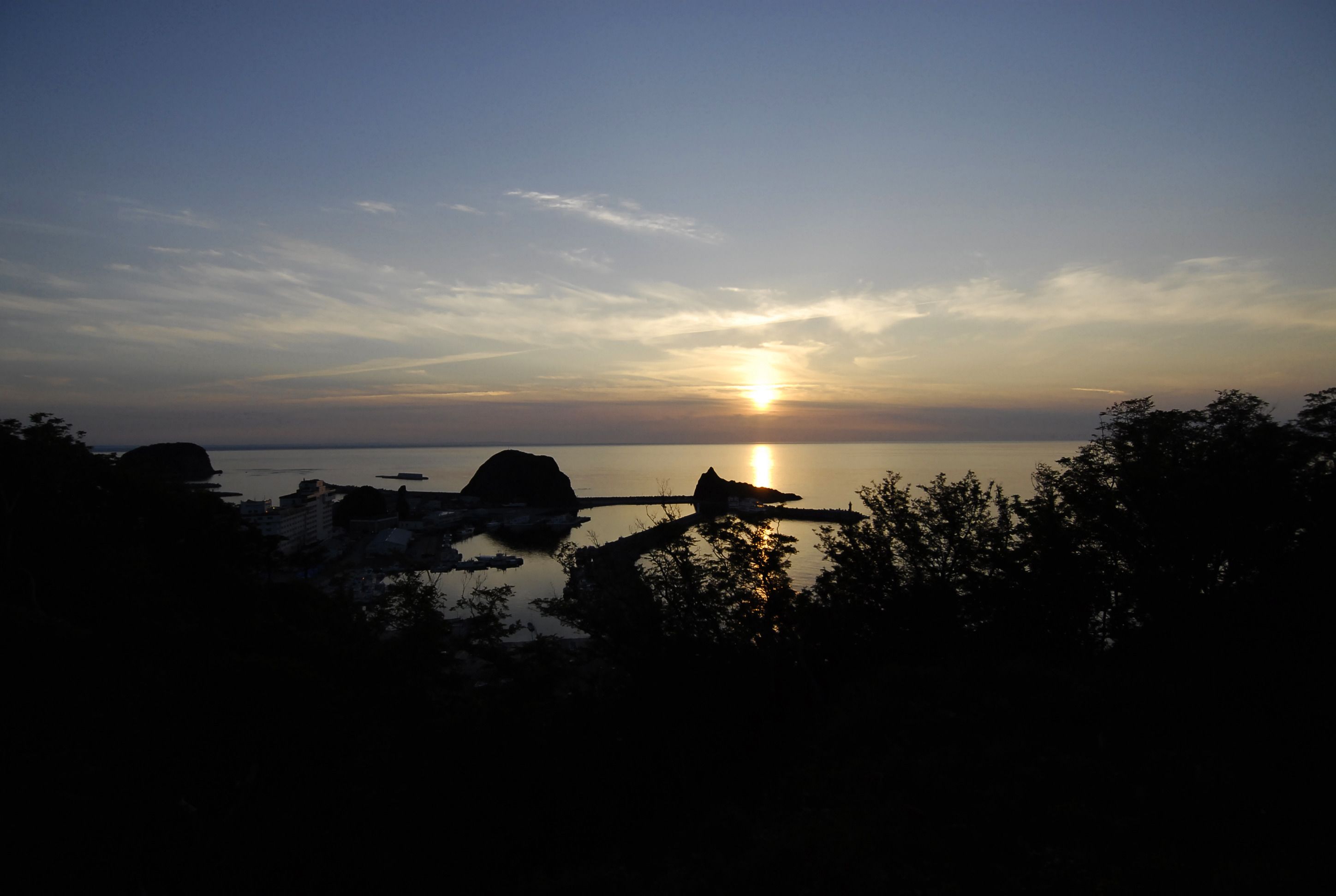 A sunset over a calm body of water with silhouettes of rocks and trees in the foreground.