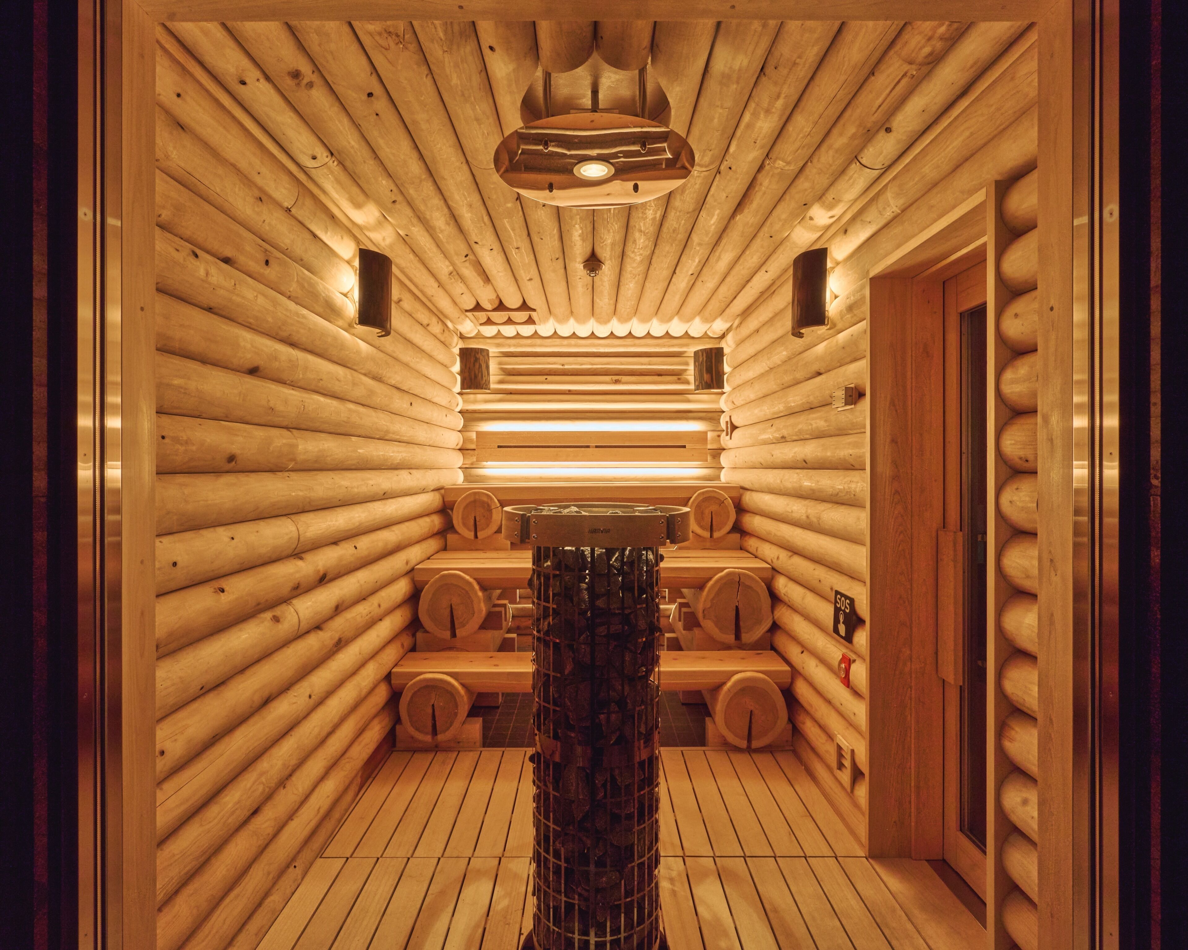 A sauna with wooden walls and benches, a central heating element, and a door on the right.