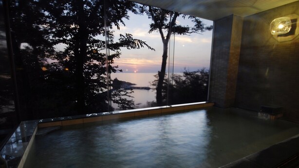 Un jacuzzi con vista a un atardecer sobre el agua, rodeado de árboles.