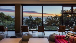 Una sala de estar moderna con ventanas amplias, una mesa de centro de madera, un sofá colorido y varias sillas.