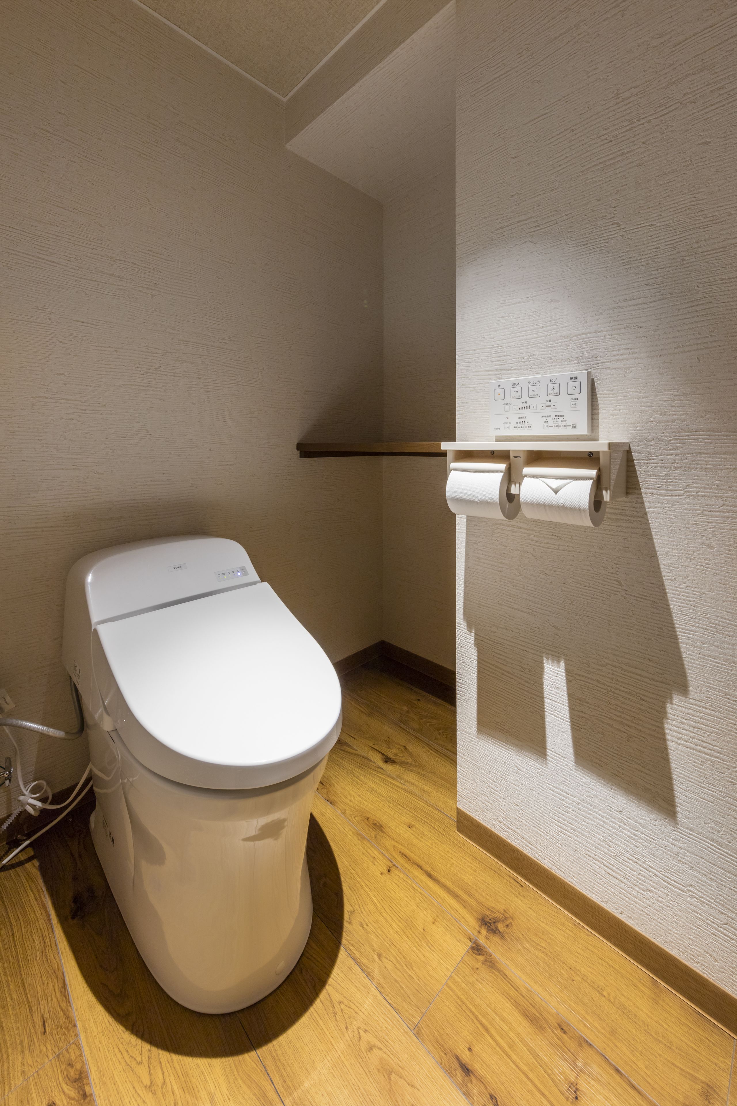 Ein kleines, modernes Badezimmer mit Toilette, Holzboden und einem an der Wand befestigten Toilettenpapierhalter.