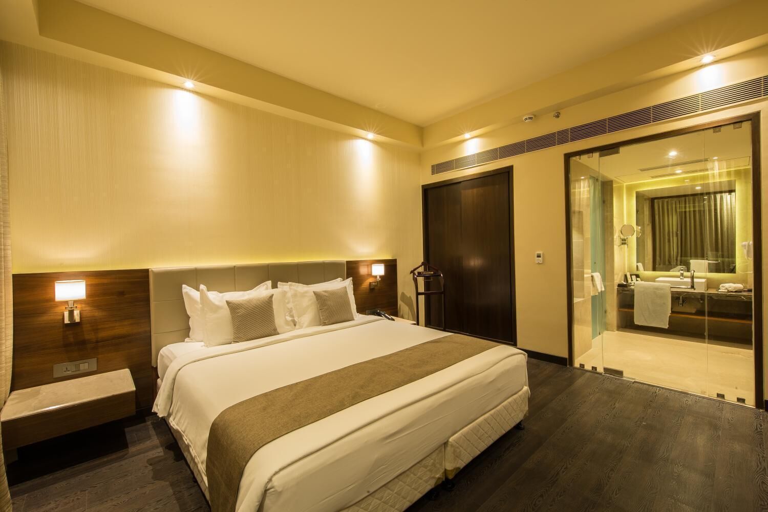 A hotel room with a large bed, bedside tables, a mirror, and a glass-enclosed bathroom.
