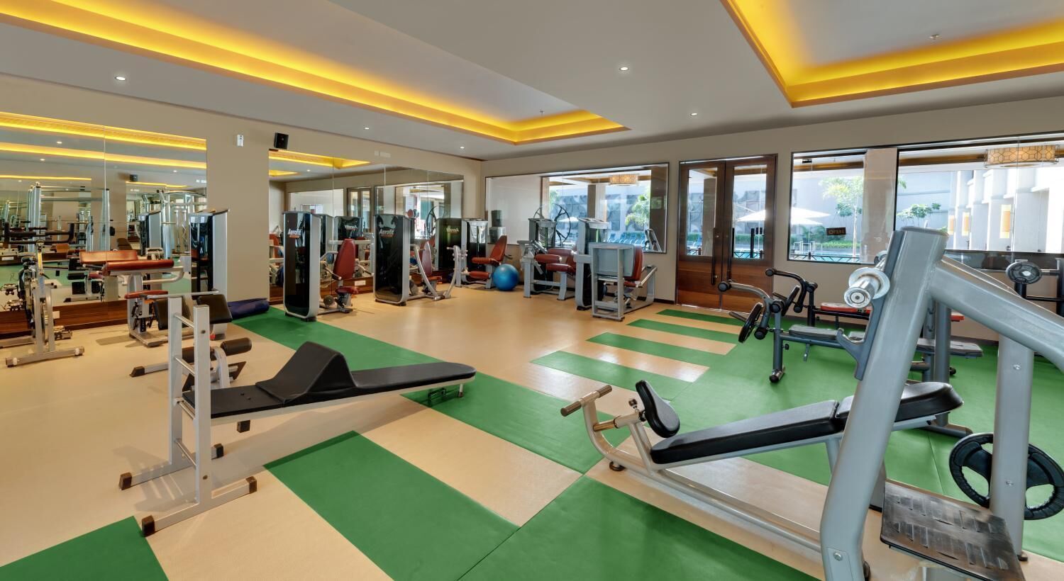 A modern gym with various exercise equipment, large windows, and a green and white floor.