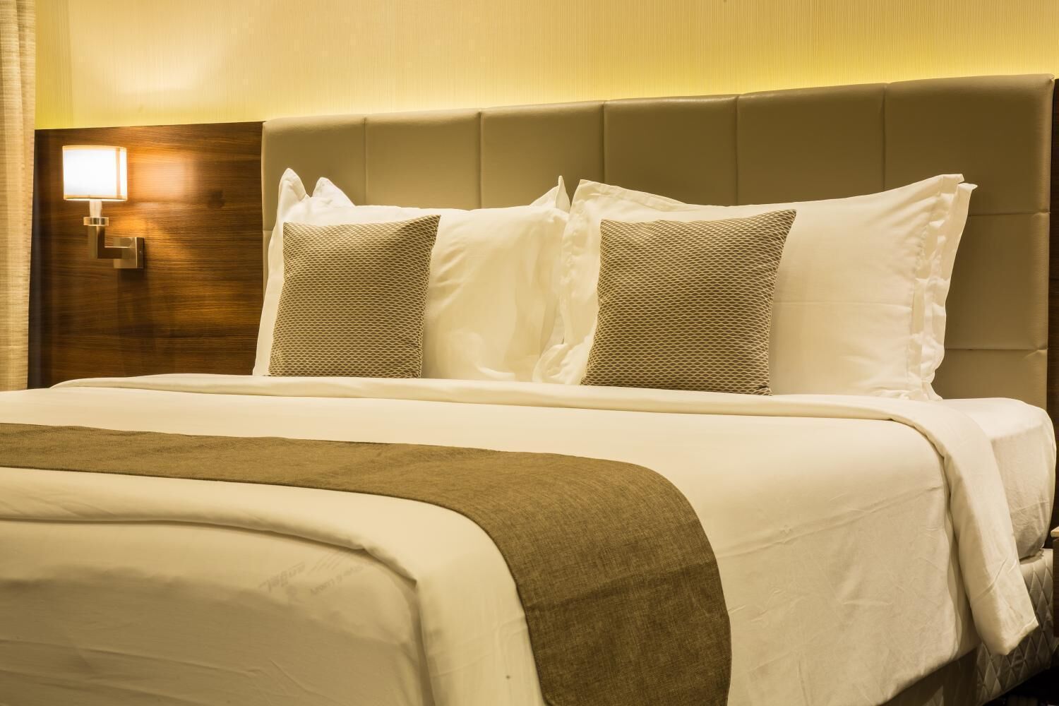 Una habitación de hotel con una cama grande, un cabecero con luz integrada y una lámpara de pared.