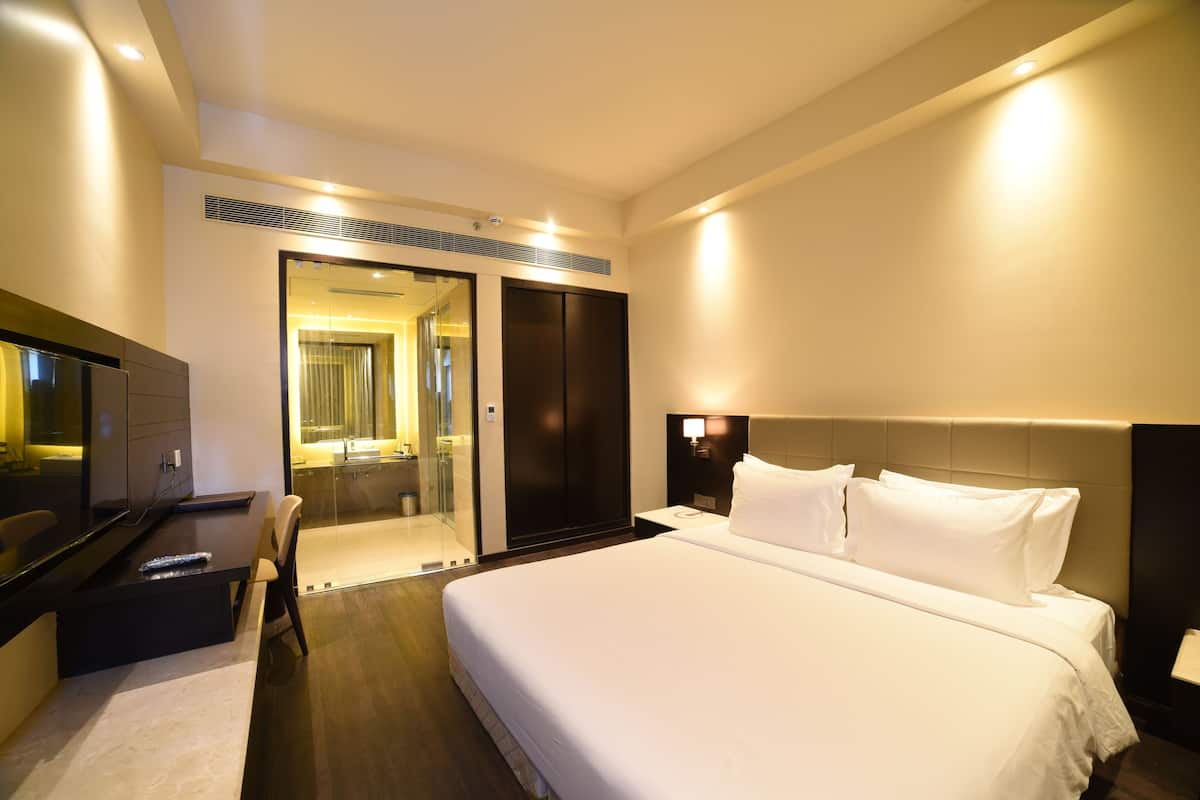 A modern hotel room with a large bed, a flat-screen TV, a desk, and a walk-in closet.