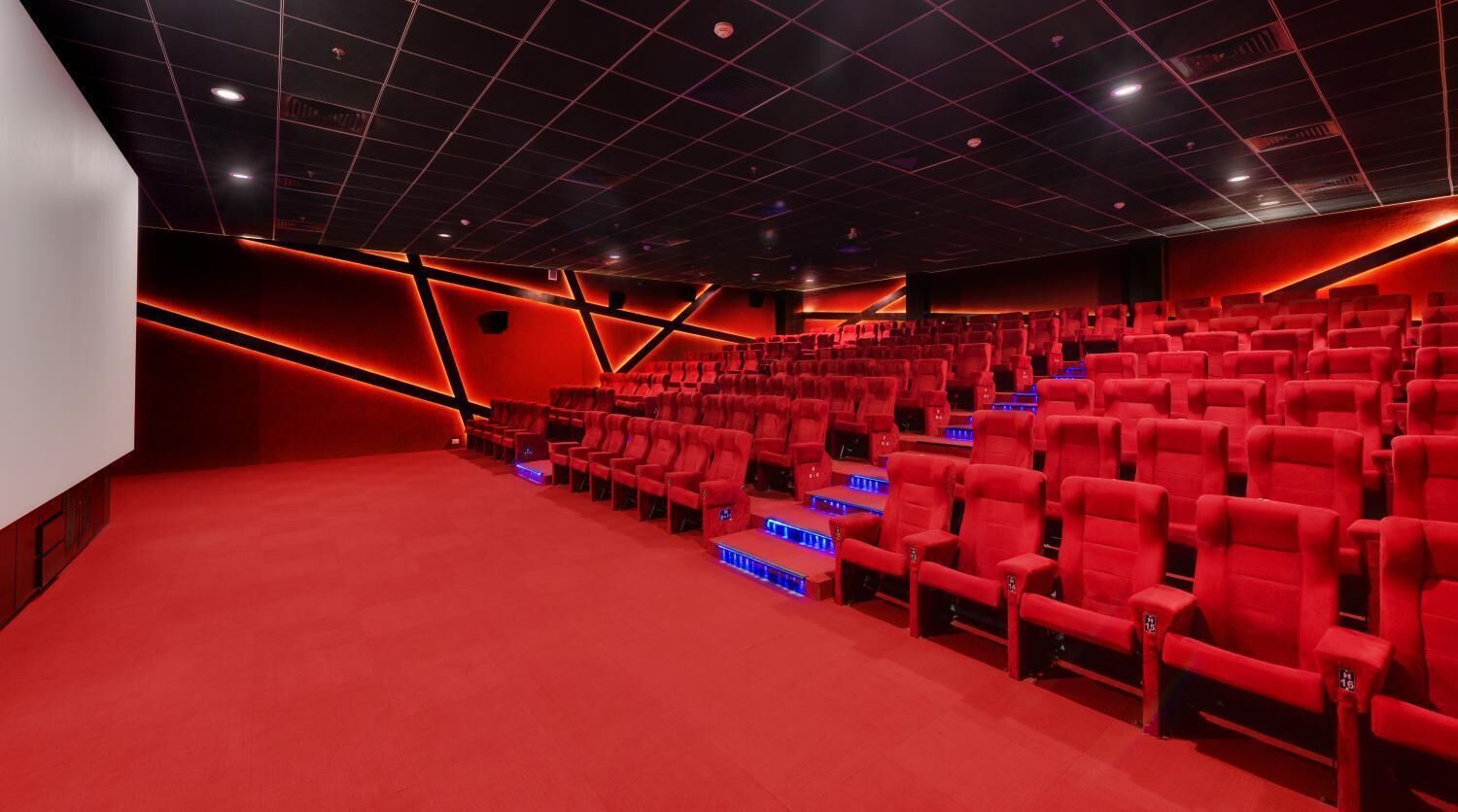 Ein Theater mit roten Sitzen, einem roten Teppich und einer deckenhohen Rasterstruktur.