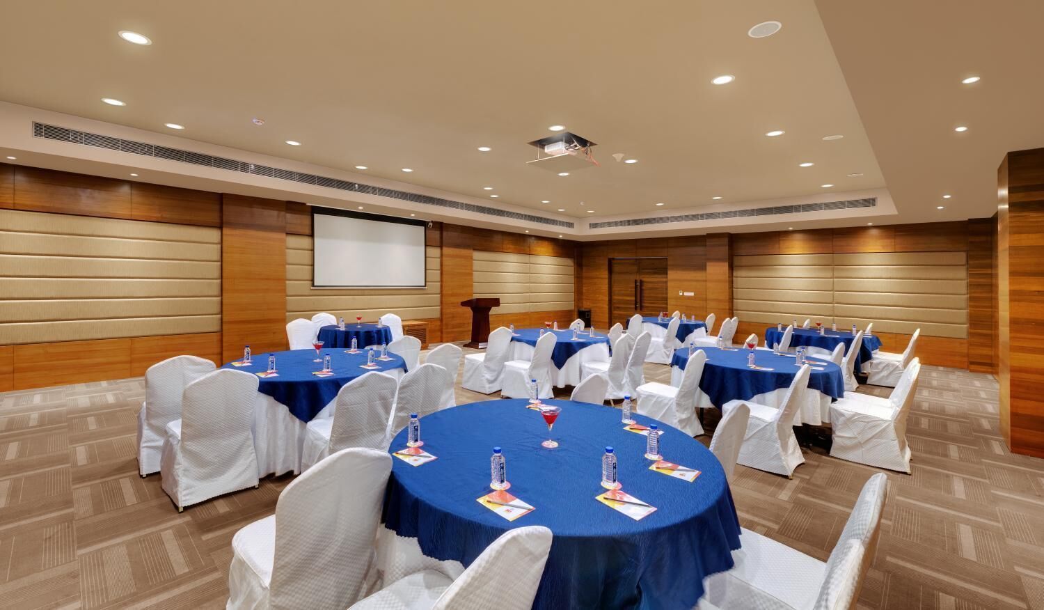 A conference room with round tables, white chairs, and blue tablecloths.