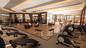 Une salle de sport équipée de matériel d’exercice, dotée d’espaces pour s’asseoir et de grandes fenêtres.