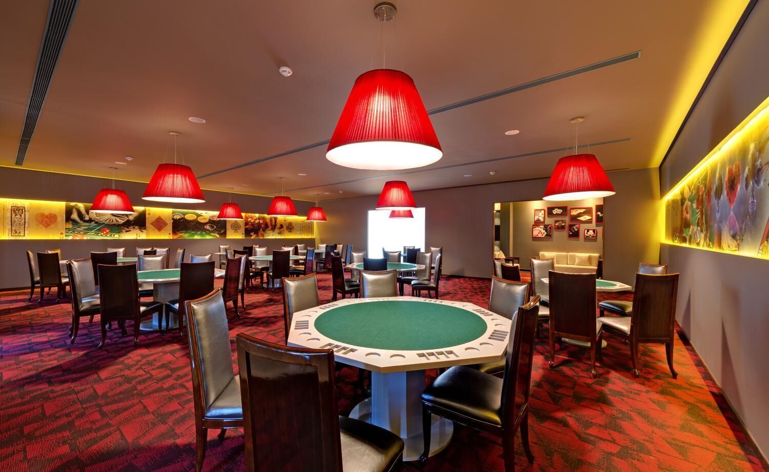 A casino with multiple blackjack tables, red pendant lights, and a red carpeted floor.