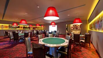 A casino with multiple blackjack tables, red pendant lights, and a red carpeted floor.