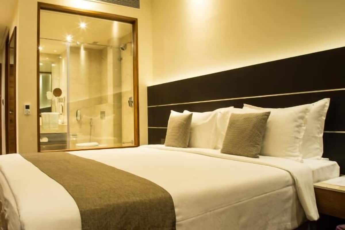 A hotel room with a large bed, a glass-enclosed shower, a wooden wardrobe, and a nightstand.