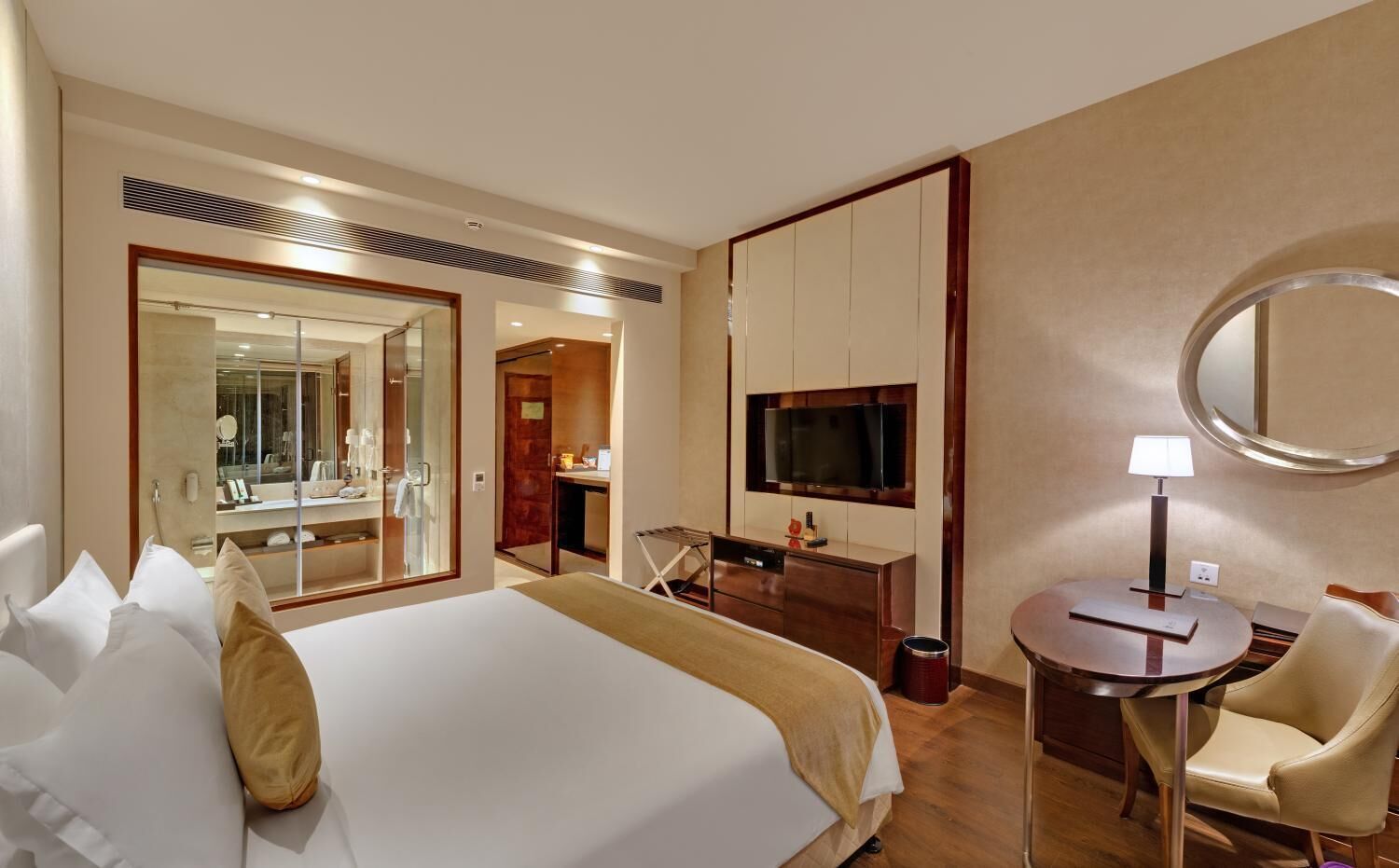 Habitación de hotel con una cama grande, un escritorio, una silla, un televisor y un espejo.