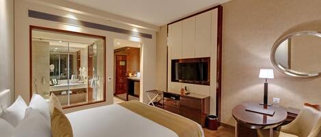 Habitación de hotel con una cama grande, un escritorio, una silla, un televisor y un espejo.