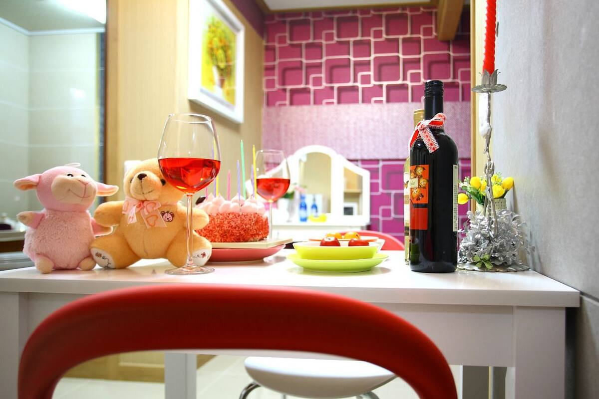Une table à manger avec des peluches, une bouteille de vin et un verre de vin rouge.