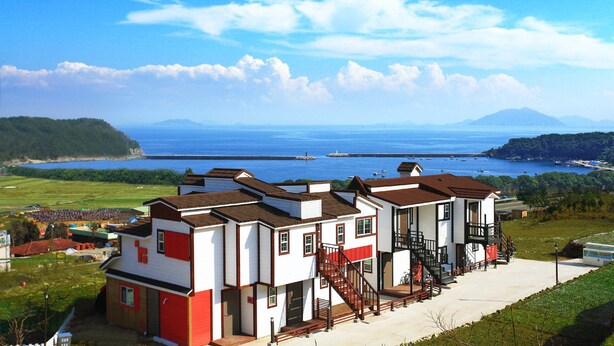A coastal building with a red and white facade, a fire escape, and a view of the sea and mountains. - Bluesean Pension (Namhae)
