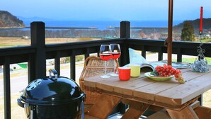A wooden table with a view of the ocean, a grill, and a wicker chair. - Bluesean Pension (Namhae)