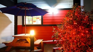 A wooden picnic table with a blue umbrella, a red wall, and a plant with red lights. - Bluesean Pension (Namhae)