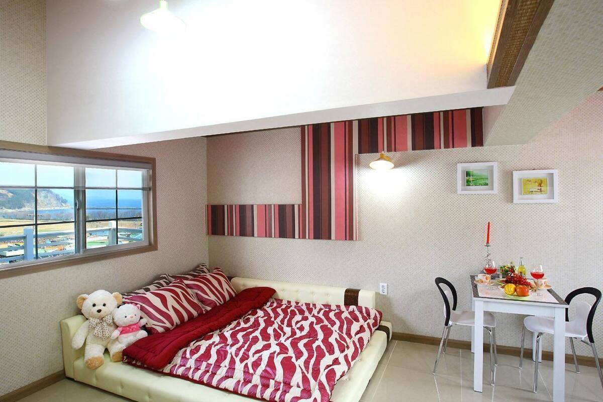Une chambre avec un lit, une fenêtre donnant sur un beau paysage, un coin repas avec une table et des chaises, et un mur décoré de motifs à rayures.