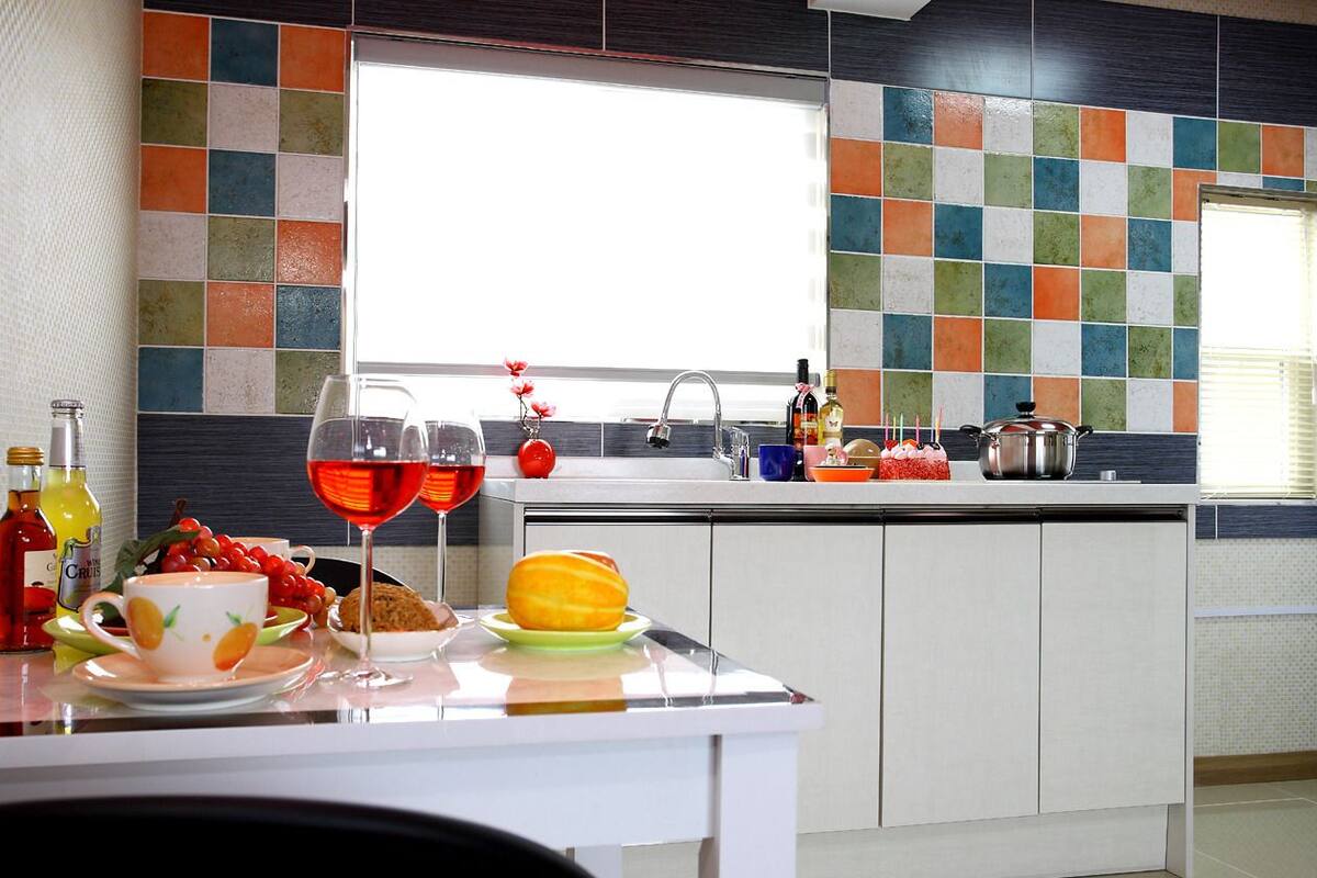 Une cuisine moderne avec un mur de crédence aux couleurs vives, un coin repas avec une table dressée pour deux personnes et une fenêtre laissant entrer la lumière naturelle.