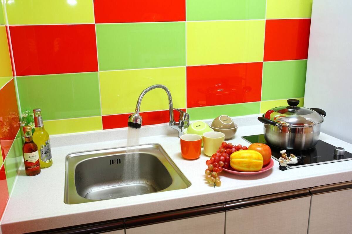 Une cuisine équipée d’un évier, d’un robinet et d’une cuisinière. On y trouve des bouteilles, un bol et une assiette remplie de fruits sur le comptoir.