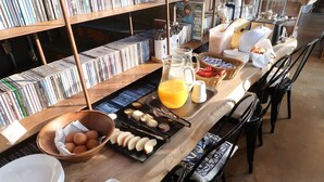 Een ontbijtbuffet met diverse gerechten, een koffieapparaat en een boekenplank vol boeken.