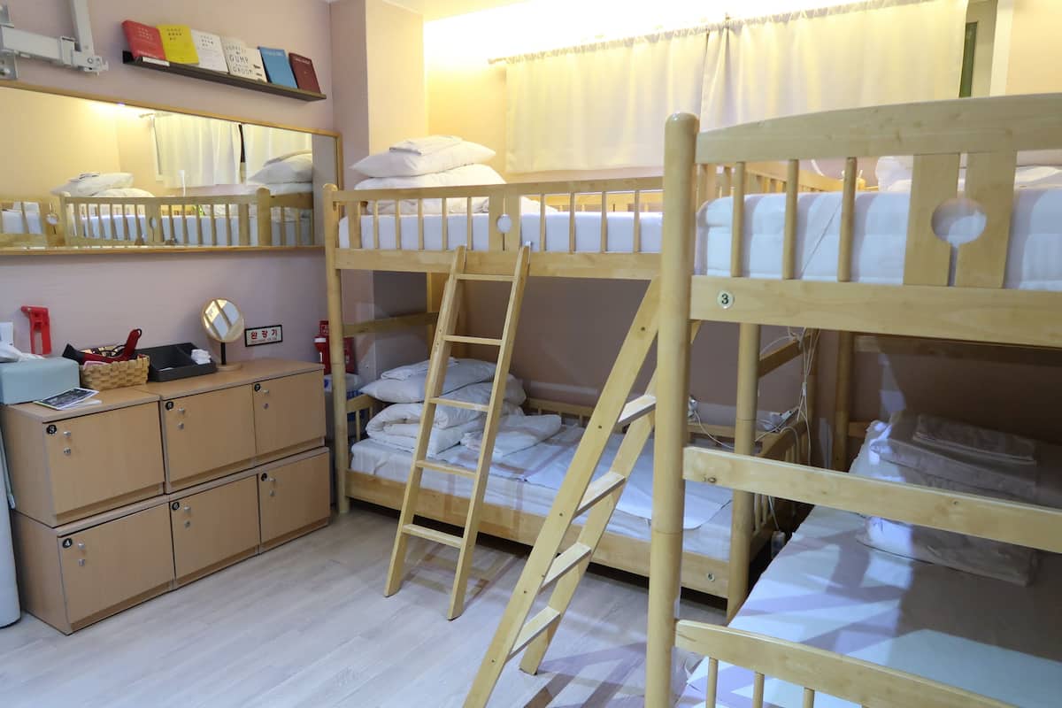 A bunk bed room with a wooden ladder and a desk with a mirror.