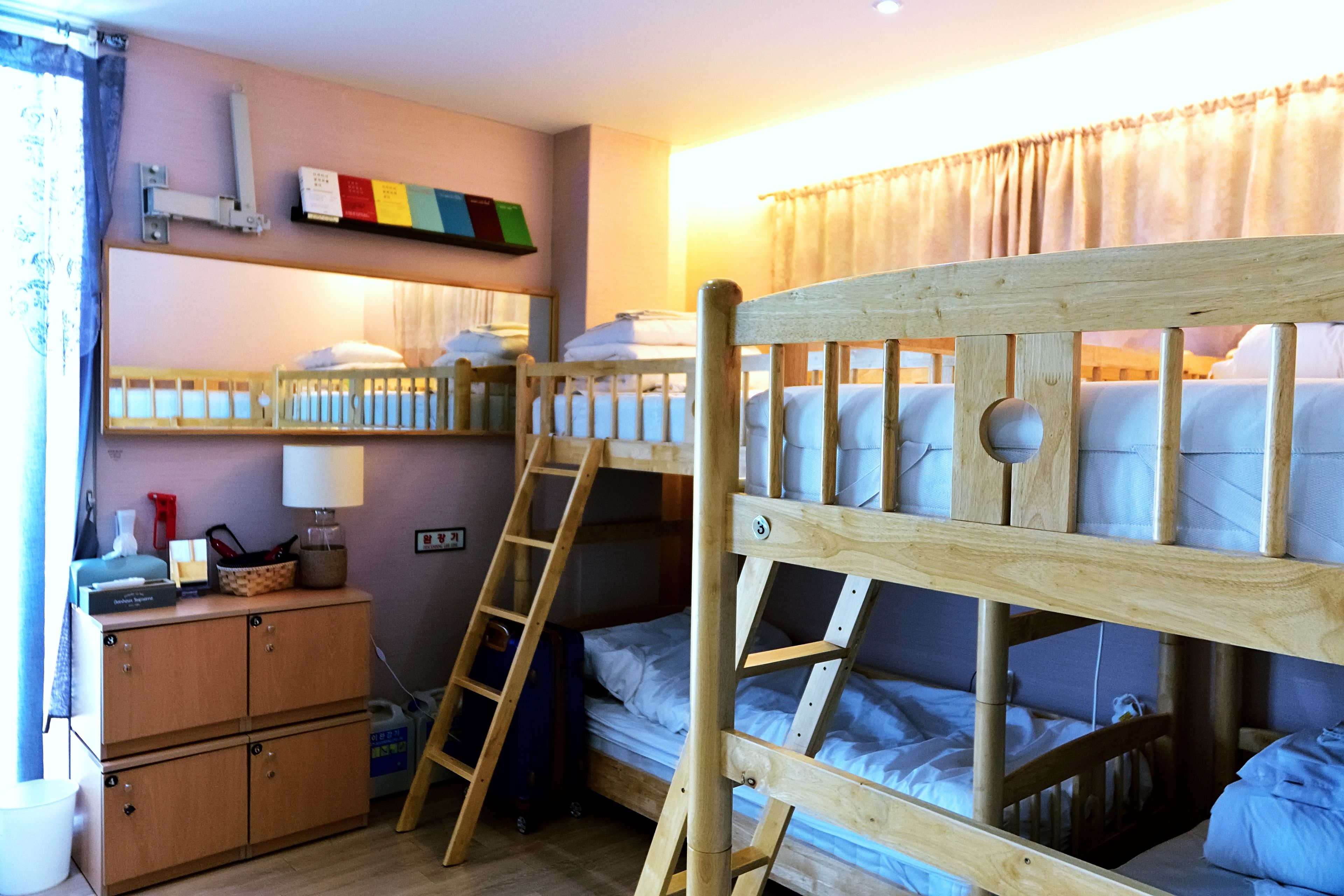 Camera con un letto a castello, una scala in legno, una piccola scrivania con una lampada e una mensola piena di libri.