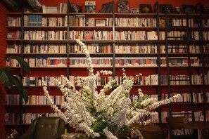 A library with bookshelves filled with books, a chair, and a white flowering plant. - Andong Poong-gyung HOSTEL n LIBRARY (Andong)