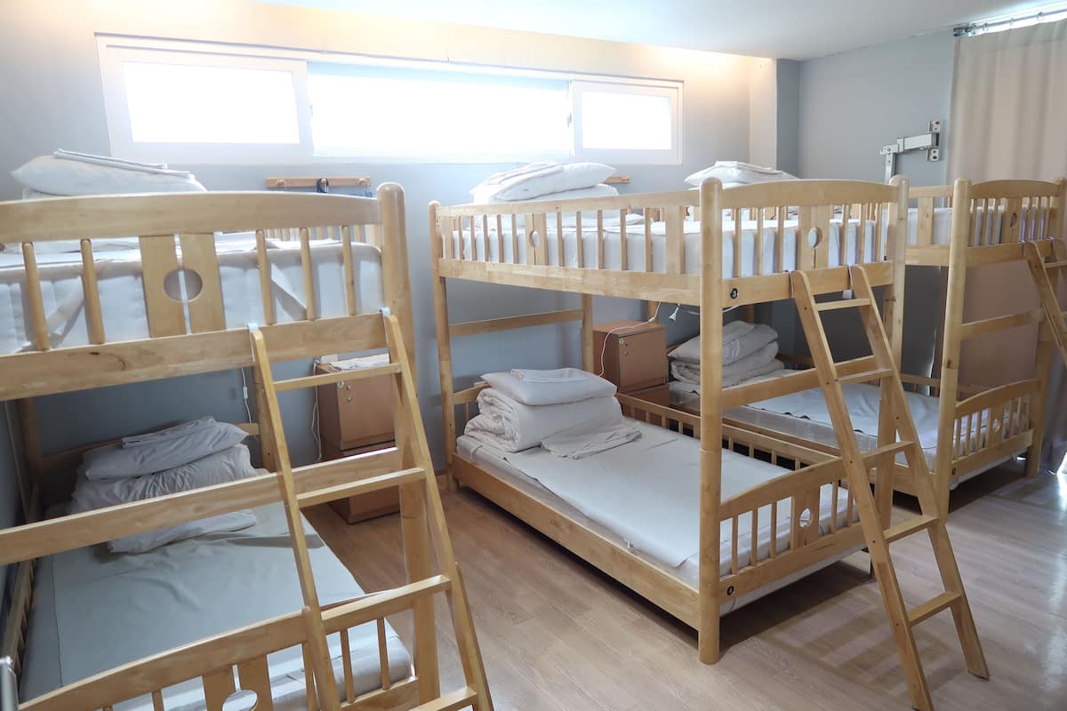 A room with bunk beds, a window with curtains, and a wooden floor.