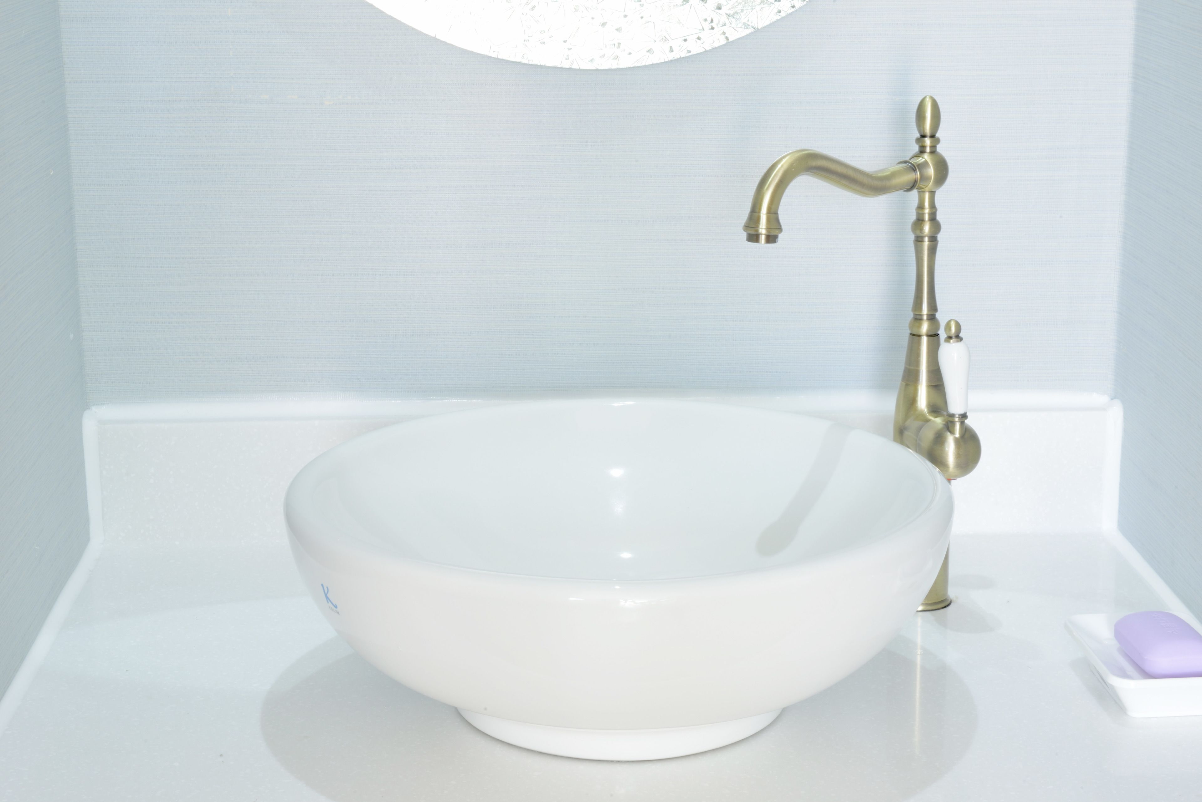 Ein weißes Keramikwaschbecken mit goldfarbenem Wasserhahn und einer Seifenschale.