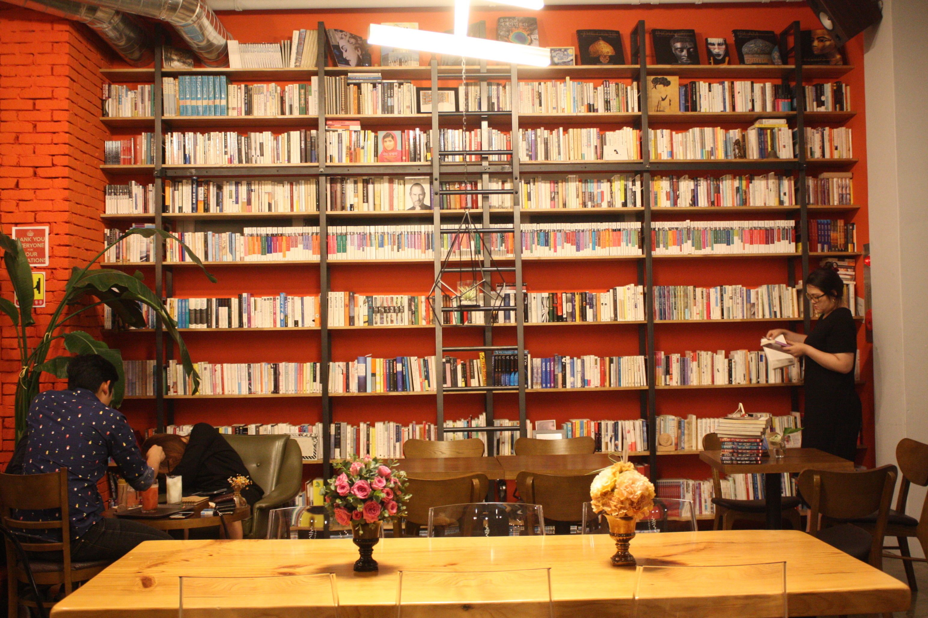 Una biblioteca con estanterías, una mesa con sillas y una persona de pie cerca de las estanterías.